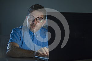 Weird tidy and neat nerd man in big glasses and shirt working happy using internet on laptop computer late night in the dark
