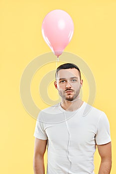 Weird young man with pink air balloon on his neck over yellow background