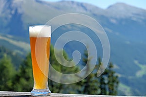 Weissbier classic best well-known Bavarian wheat beer in a German Hefeweizen glass on wooden table. Mountain ranges( photo
