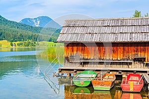 Three colourful fishing boats and wooden cabin on shore of Weissensee lake in summer landscape of Carinthia land, Austria