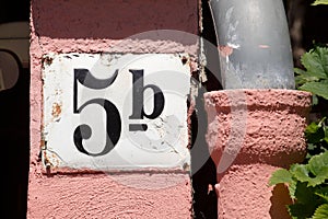 Weisses Hausnummernschild Nr. 5b auf rosa Hauswand, Abflussruhr,