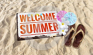 Welcom summer sign on sandy beach with jute slipper and flower with paper umbrella photo