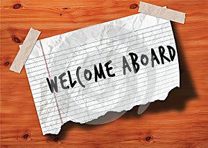 WELCOME ABOARD handwritten on torn notebook page crumpled paper on wood texture background.