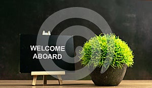 WELCOME ABOARD wrote on chalkboard with green plant in pot