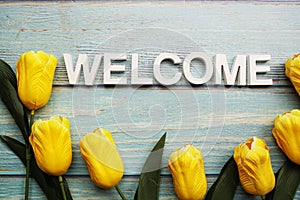 Welcome alphabet letters with yellow tulip flower on wooden background