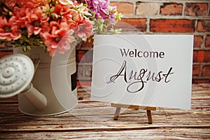 Welcome August text with flower bouquet decoration on wooden and old brick wall background