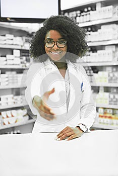 Welcome back sir. Portrait of a cheerful young female pharmacist reaching out to shake hands while looking at the camera