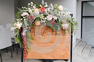 A welcome board sign with a beautiful flower decoration, standing in front of wedding entrance