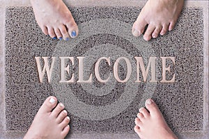 Welcome Door Mat With Funny Family Feet. Friendly Grey Door Mat Closeup with Four Bare Feet Standing. Four Feet on