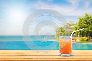 Welcome drink orange juice punch put on wooden table nearly swimming pool with blue water and blue sky in background.