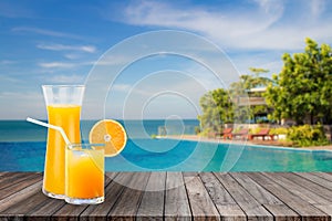 Welcome drink orange juice punch put on wooden table nearly swimming pool with blue water and blue sky in background.