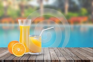 Welcome drink orange juice punch put on wooden table nearly swimming pool with blue water and daybed in background.