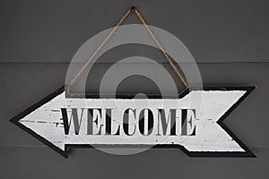 Welcome inscription on arrow sign. Rustic vintage pointer on wall photo closeup. Weathered wooden texture, welcome word