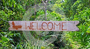 Welcome inscription by red paint on wooden board, green tropical garden background