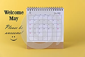 Welcome May. Please be awesome. With May 2022 desk calendar and happy smile emoticon on yellow background.