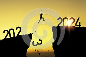 Welcome merry Christmas and happy new year in 2024,Silhouette Man jumping from 2023 cliff to 2024 cliff with yellow sky and