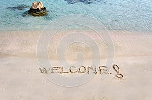 Welcome message written on white sand, with tropical sea waves in background