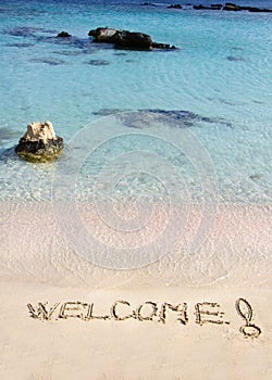 Welcome message written on white sand, with tropical sea waves in background