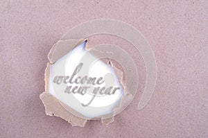Welcome new yearword in hole ripped on brown paper. Copy space