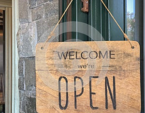 Welcome, we are open sign on the door of the store/cafe. Wooden board with text. Business after quarantine concept.