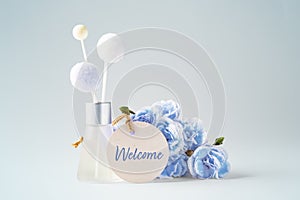 Welcome paper tag with fragrance diffuser and flowers on vintage blue background