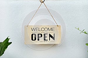 Welcome we`re open. black text on wood sign hanging on white wall