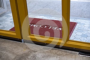 Welcome red mat greeting all visitors in front of a yellow glass door for  shop and restaurant in a shopping mall.