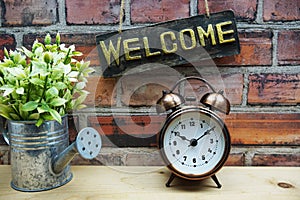 Welcome sign hanging with alarm clock on old brick wall background