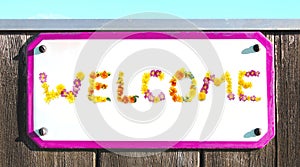 WELCOME sign made of yellow pink red and orange flowers collage, enamel, metal or pottery sign, wooden wall. frame, turquoise sky