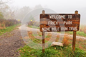 The Welcome to Frick Park Nine Mile Run Trail sign on a foggy fall morning in Pittsburgh, Pennsylvania