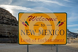 Welcome to New Mexico road sign with an overcast sky and mountains in the background.