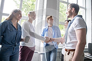 Welcome to our team! Business men in smart casual wear shaking hands while working in the creative office.