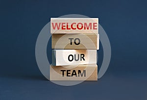 Welcome to our team symbol. Wooden blocks with words `Welcome to our team` on beautiful grey background. Businessman hand.