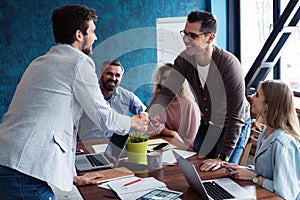 Welcome to our team! Young modern men in smart casual wear shaking hands while working in the creative office.