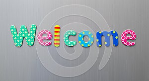 Welcome word spelled out in bright colorful patterened letters on brushed metal background photo