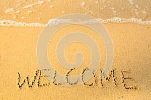 Welcome, written in sand on beach texture, soft wave of the sea. Travel.