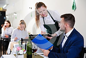 Welcoming female waiter is taking order from businessman in restaurante