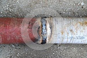 A welded butt joint with some defects. Red and white metal pipes welded together