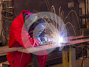 Welder bends to cut metal beam with orange sparks. photo