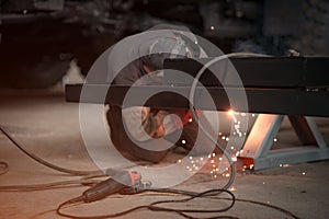 A welder in a car workshop will weld a truck frame. Near the worker lies the grinder tool. Focus on the grinder