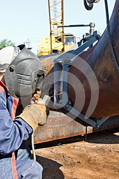 Welder in coveralls makes a weld on a pipe of large diameter