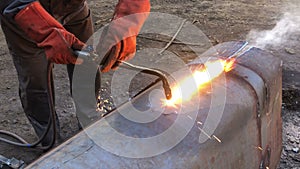 The welder cuts large metal pipes with ocetylene welding. A worker on the street cuts large-diameter pipes during the