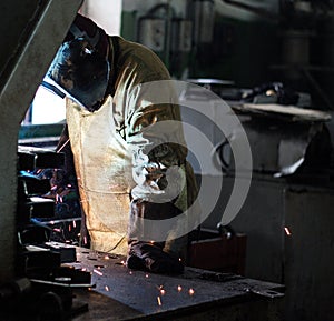 Welder at the factory in a welding mask welds metal parts, welding and sparks, electrode, workshop