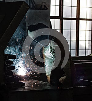 Welder at the factory welds metal parts, welding and sparks, dirty production, harmfulness