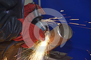 Welder hands grinding metal piece with a grinder, processing weld after welding, workshop