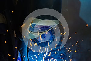 Welder in the helmet works in the shop. Bright sparks from metal welding.