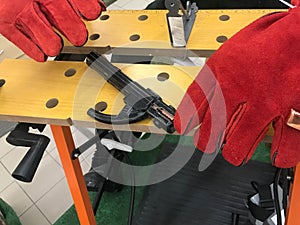 A welder man in red work gloves is working and holding an electron and clamps for welding at the table