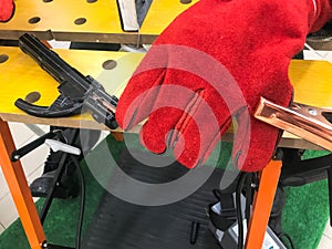 A welder man in red work gloves is working and holding an electron and clamps for welding at the table