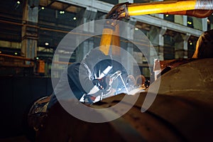 Welder in mask works with metal pipe on factory