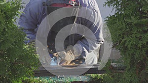 Welder of metal welding with sparks and smoke in a private garden.